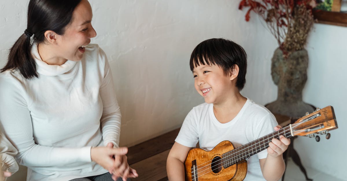 Hawaiian Airlines Boarding/Deboarding Music - Positive ethnic child sitting with traditional Hawaiian musical instrument and looking away near content mother sitting with open mouth near vase with decorative branch