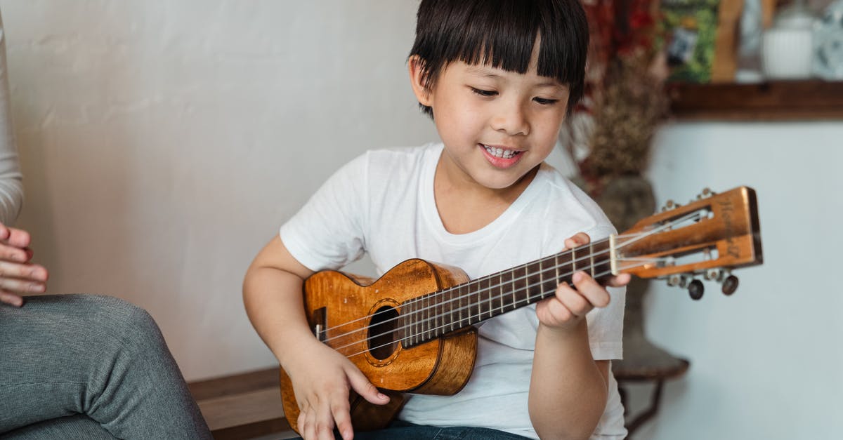 Hawaiian Airlines Boarding/Deboarding Music - Content ethnic child in casual wear playing traditional Hawaiian musical instrument while sitting near crop faceless person at home in daylight