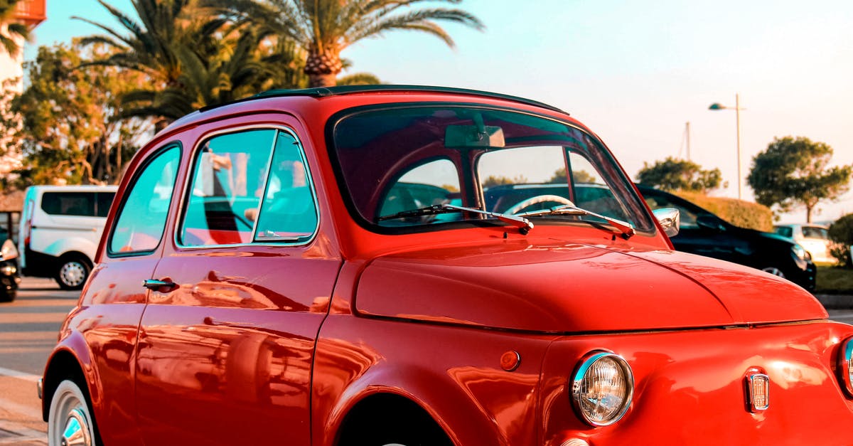 Hazards on road trip through Italian Alps - Vintage small red car parked on roadside near tropical palm trees against cloudless blue sky