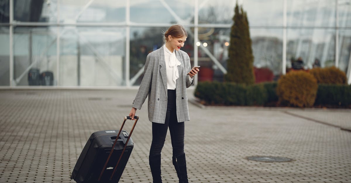 Heathrow airport Terminal 3 connection - Smiling female passenger with suitcase messaging on mobile phone in street