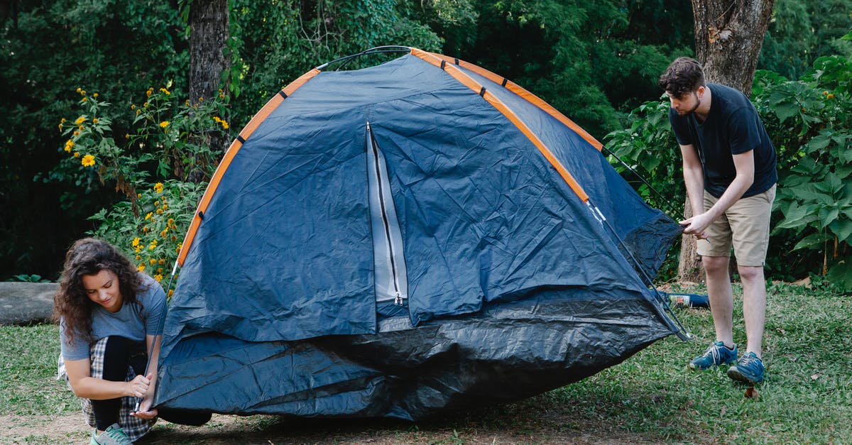 Help for a first-time traveller - Couple of travelers setting up tent on meadow against trees and bushes during summer journey in daylight