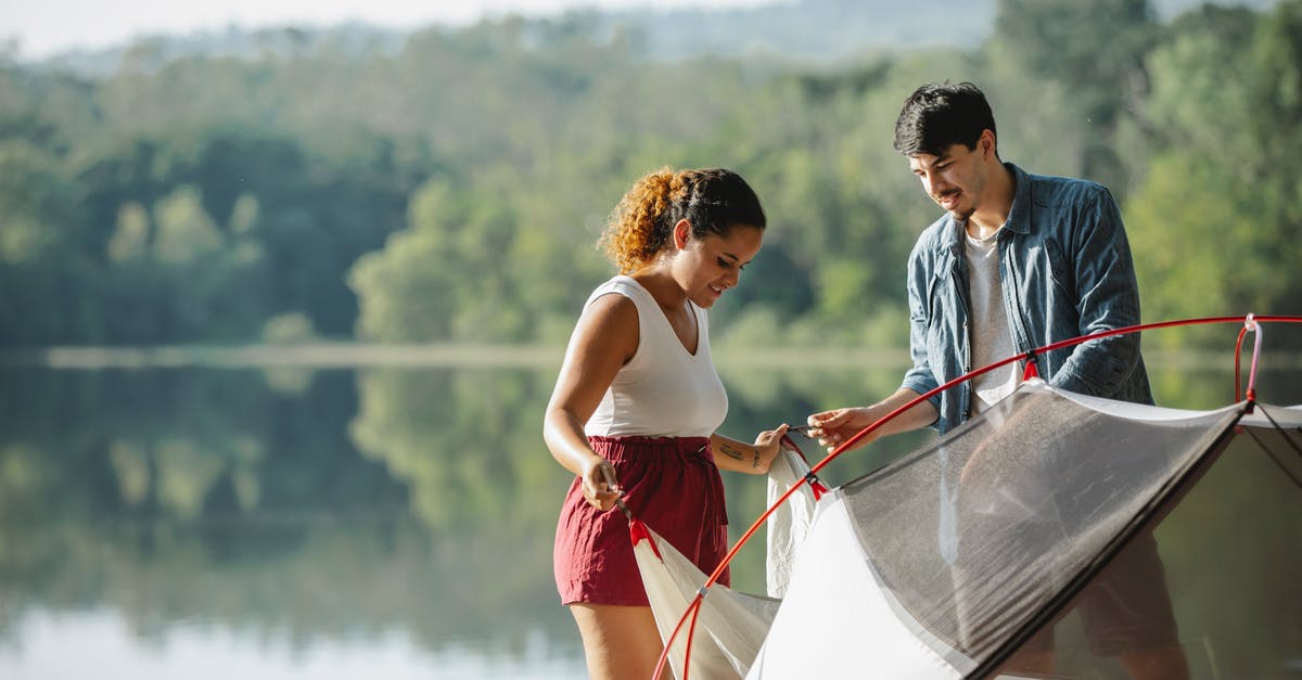 Help for a first-time traveller - Multiracial couple of tourists setting up tent against river