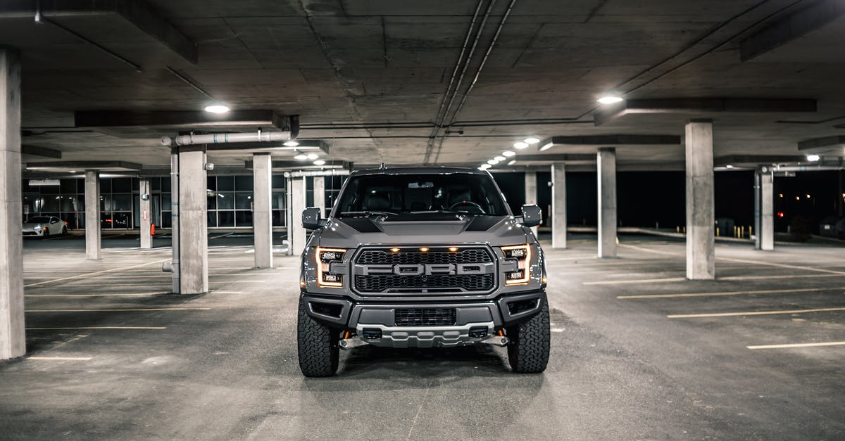 Hertz@SFO: Park during car pickup - Modern gray pickup with glowing headlights parked on asphalt in underground parking lot with columns in evening time in city