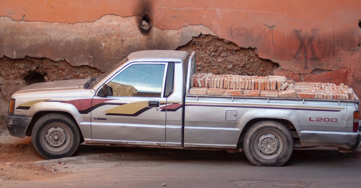 Hertz@SFO: Park during car pickup - Old pickup car with heap of bricks in trunk parked on town street near shabby old building on sunny day