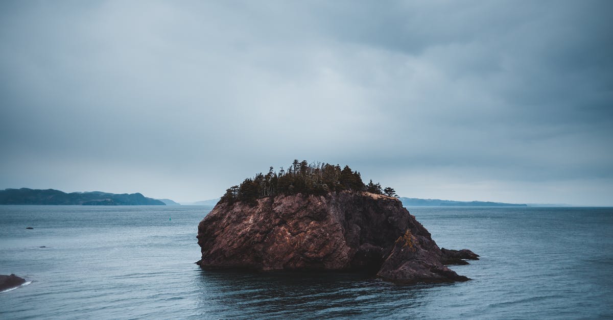 Hiking trails on Bainbridge Island to see the skyline of Seattle? - Amazing scenery of rocky uninhabited island in rippling sea located in Chance Cove coastal town against cloudy gray sky