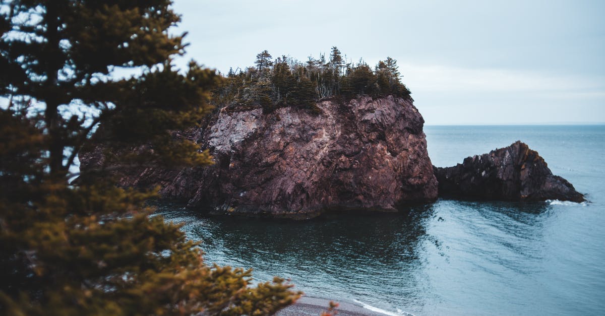 Hiking trails on Bainbridge Island to see the skyline of Seattle? - Spectacular scenery of rocky formation in ocean with trees on peak and empty beach surrounded by evergreen forest located in Chance Cove coastal town on cloudy day