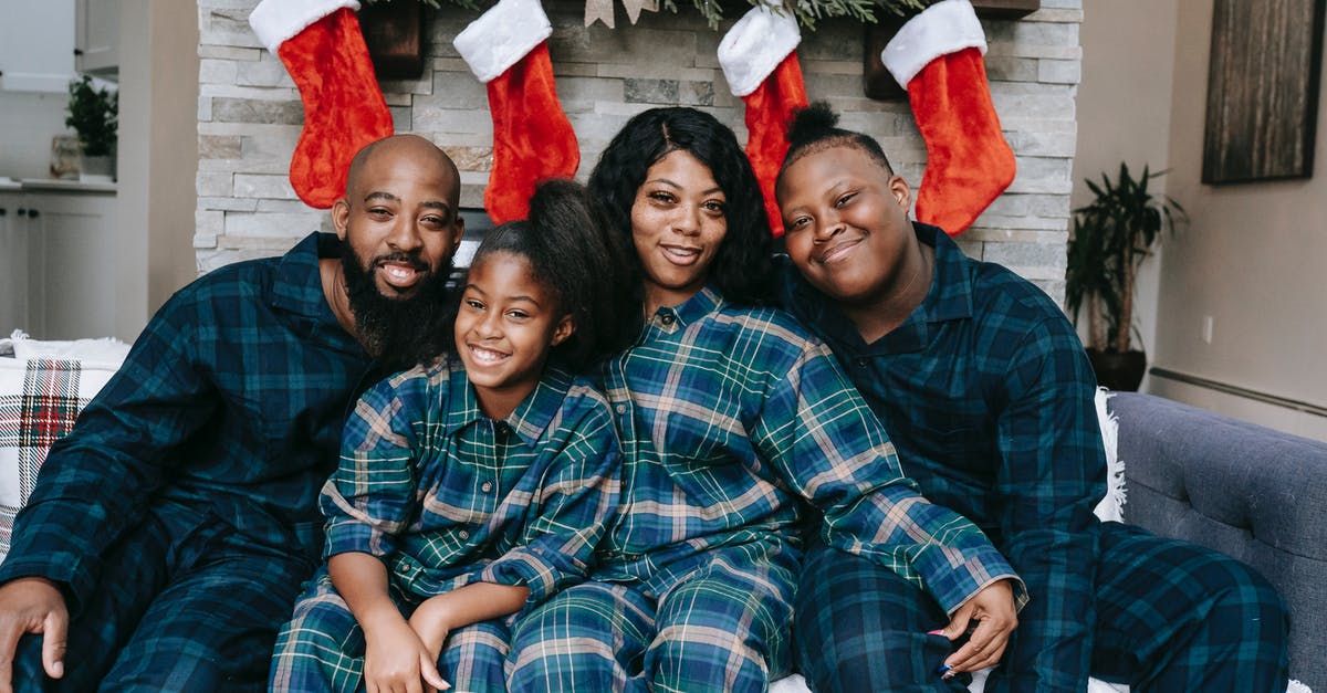 Hiking with children close to Prague, Czechia in winter - Cheerful African American family wearing similar clothes sitting close at home decorated with Christmas gift socks