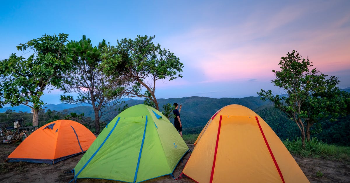 Hill walking and camping in the Peak District - Colorful tents located at camp in mountainous valley near green trees against picturesque sunset sky