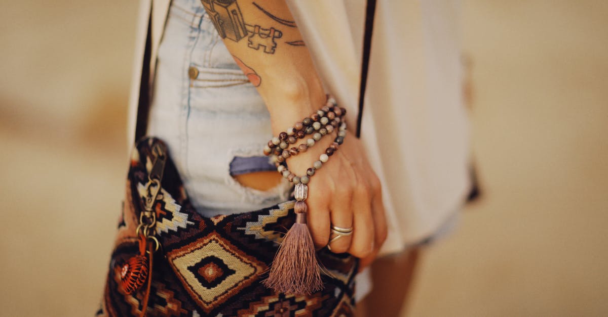 Hitchhiking through Native American reservations - Unrecognizable Female Hand with Tattoos and Bracelet and Figured Shoulder Bag