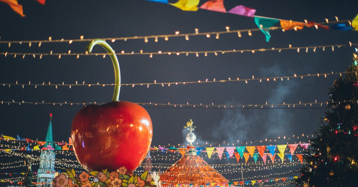 Holiday in Uk from Russia [closed] - Big red glossy toy apple on roof of building on fairground against dark sky in evening city park decorated to winter holidays