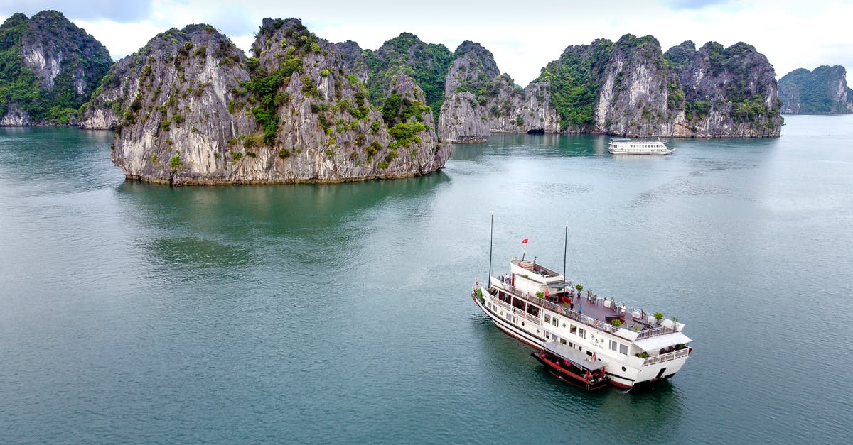 Holiday on Cruise Ship [closed] - Height view of cruise vessel sailing in calm ocean to big rocks overgrown with green plants in daylight