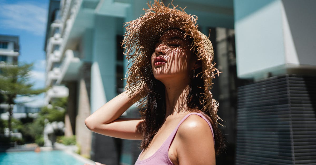 Hotel bookings for Schengen traveller [closed] - Side view of self assured young ethnic female traveler in trendy straw sunhat enjoying sunny day with closed eyes while relaxing at poolside in modern resort