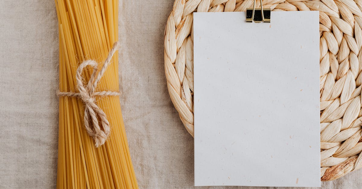 How am I supposed to combine items from Italian restaurant menus? - From above of blank paper placed on wicker table mat next to spaghetti tied with bow arranged on table covered with linen tablecloth suitable for recipe or ingredient listing