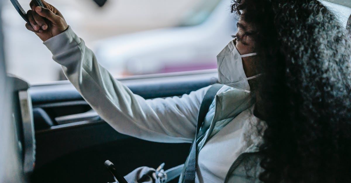 How are connection complications on a single KLM+Kenya Airways itinerary handled? - Side view of anonymous young African American female passenger in casual clothes and protective mask holding handle and looking away while sitting on backseat of taxi with smartphone in hand