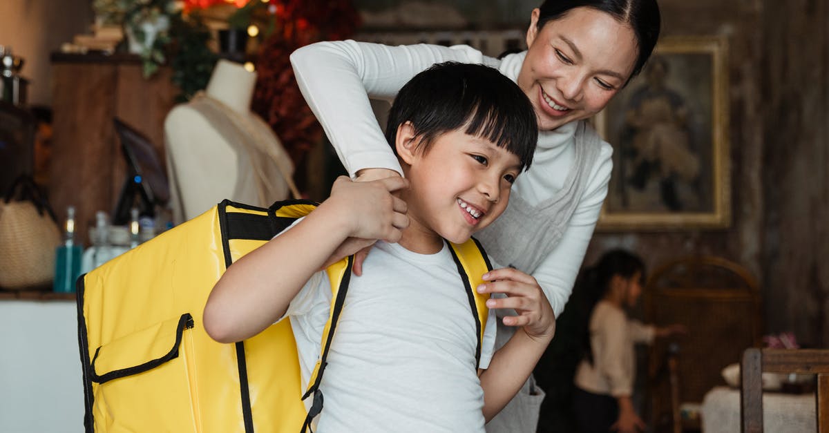 How big of a backpack should I buy? (Trans-Mongolian) - Happy female cafeteria employee putting on big yellow thermo bag on shoulders of positive child in casual wear working as food courier and looking away