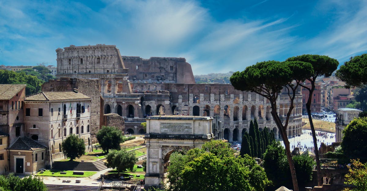 How busy is the Roman Colosseum throughout the year? - From above of aged masonry Colosseum and ancient arch near trees under bright blue cloudy sky in Italy