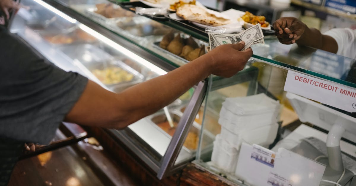 How can a tourist order a dabbawala lunch? - Crop faceless person standing near checkout buying food and passes money for dinner in cafe