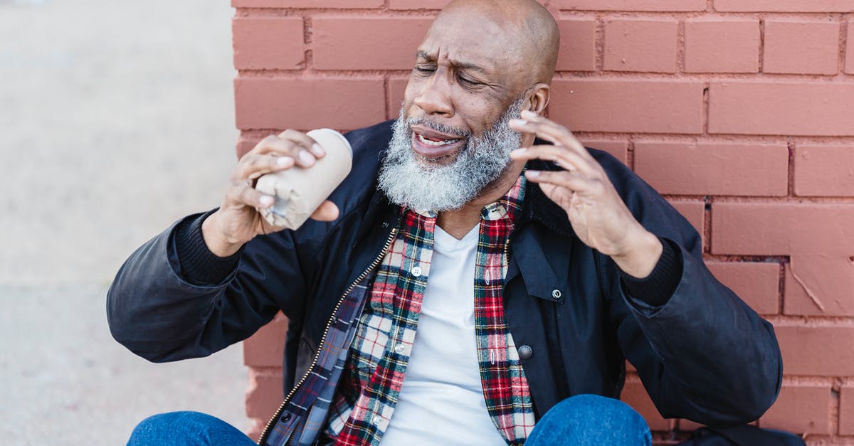 How can I avoid being shown in a border control reality show? - African American bearded male in casual outfit raising arms with beer can while resting on street near brick wall