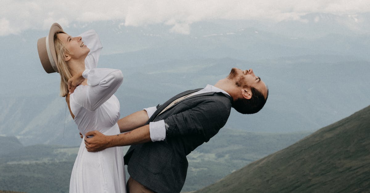 How can I find a guide that will take me safely up Mount Kilimanjaro and Mount Elbrus? - Side view of cheerful trendy groom embracing elegant bride in hat while looking up against mounts under cloudy sky