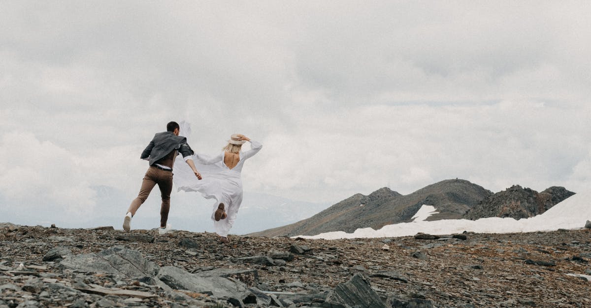 How can I find a guide that will take me safely up Mount Kilimanjaro and Mount Elbrus? - Back view of unrecognizable trendy groom catching up bride in white dress on ridge with snow on wedding day