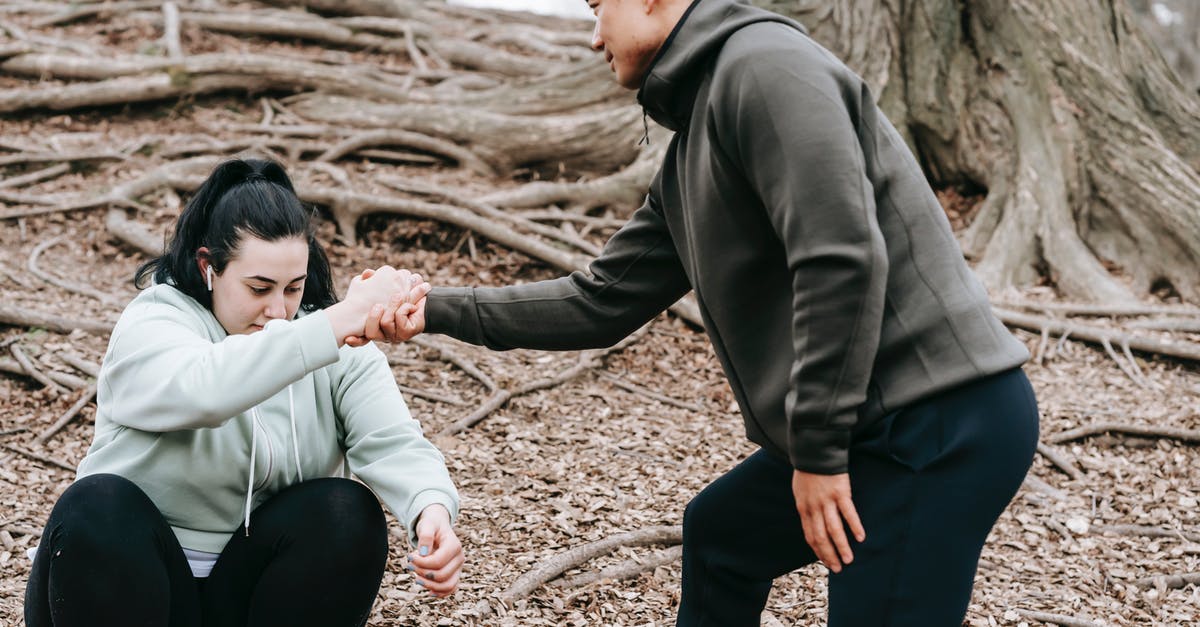 How can I get help understanding UK visa requirements? - Ethnic man in sportswear helping overweight female with dark hair get up from ground in park in daytime