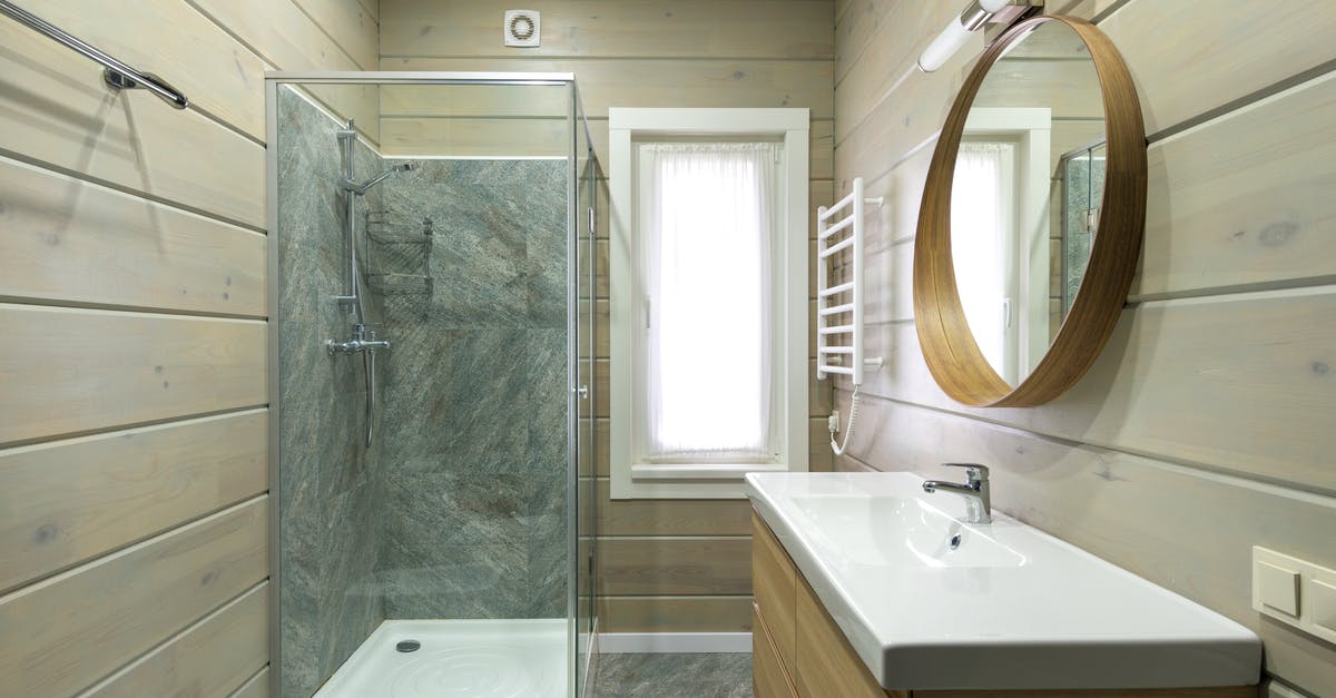 How can I know in advance if a private bathroom is not en suite? - Contemporary bathroom design with round mirror hanging above sink and shower cabin near window and paneled walls