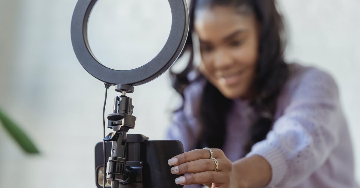 How can I live and work in the UK? [closed] - Cheerful young African American female blogger in stylish sweater smiling while setting up camera of smartphone attached to tripod with ring light before recording vlog