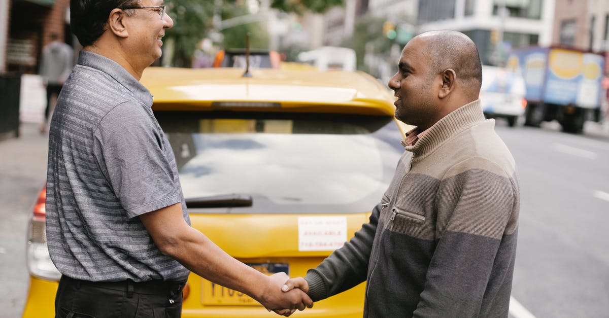 How can I meet the world's most jovial taxi driver? - Side view of smiling ethnic men shaking hands and greeting each other while standing on street near taxi car