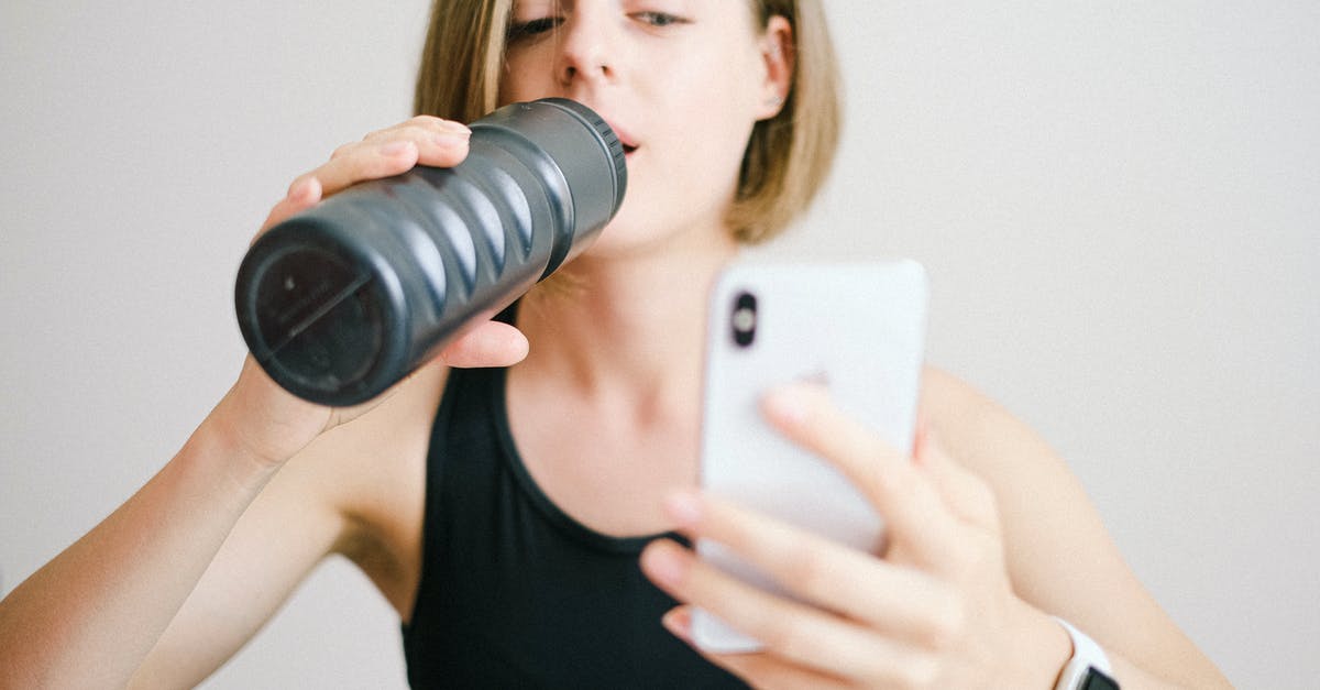 How can I secure my online activity while traveling? - Woman in Black Tank Top Holding White Smartphone While Drinking