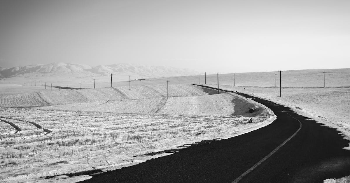 How can I travel to the North Pole, cheaply? - Black and white of empty asphalt roadway running through mountainous terrain with fields covered with snow