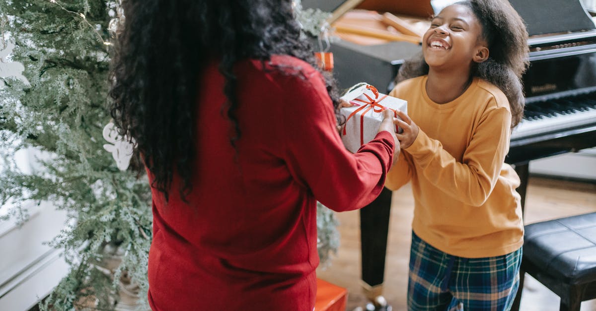 How can you identify the year of a boarding pass - Crop anonymous black woman passing gift box to cheerful daughter during New Year holiday at home