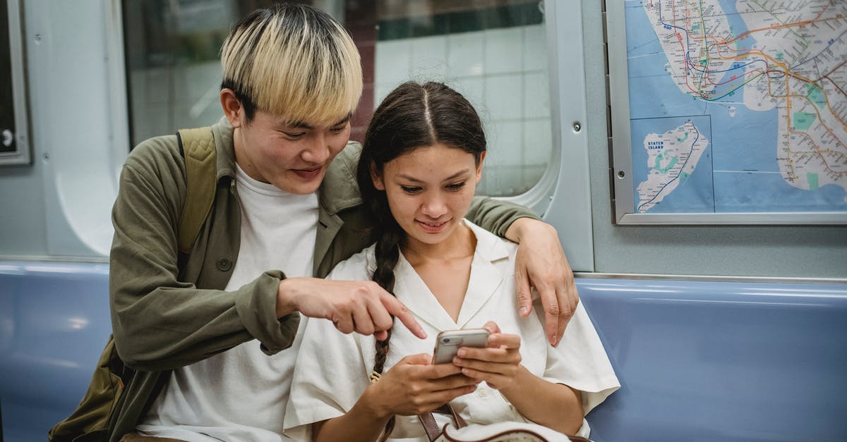 How close can one get to Eldborg with public transportation? - Happy young trendy Asian guy hugging smiling girlfriend and pointing at smartphone screen while commuting by subway train How close can one get to Eldborg with public transportation? - Happy young trendy Asian guy hugging smiling girlfriend and pointing at smartphone screen while commuting by subway train