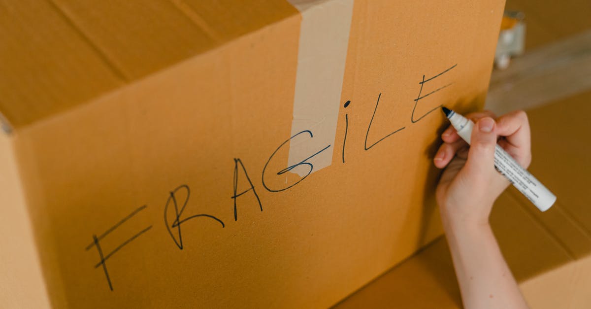 How could I receive a Parcel from Germany at Lithuanian Parcel Station? - From above of crop unrecognizable person writing with marker on cardboard box with fragile products before relocation