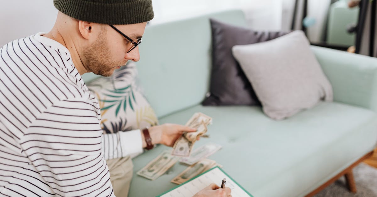 How do I keep my cash safe in Japan? - Man Writing on a Paper While Sitting on Green Couch 