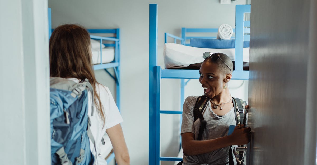 How do you 'self-isolate' in a hostel dorm room? - Woman in Gray and Black Tank Top Standing Beside Blue Metal Bed Frame