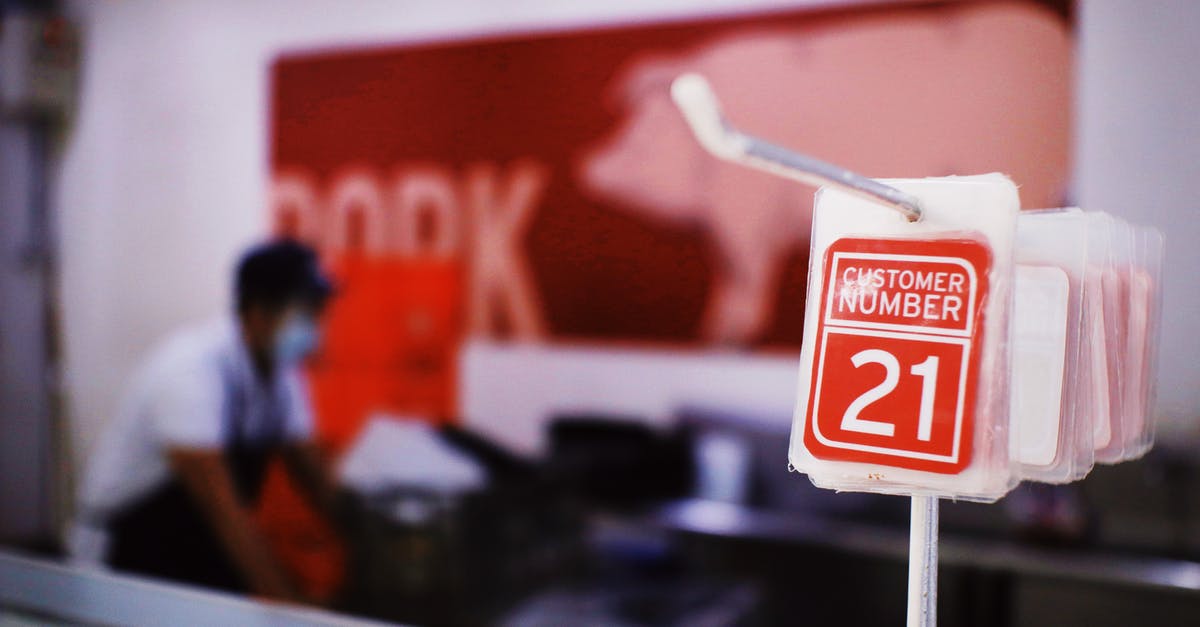 How do you call a local service number, when abroad? - Cards with customer numbers hanging on metal rack against blurred seller standing near counter with pork meat in local market