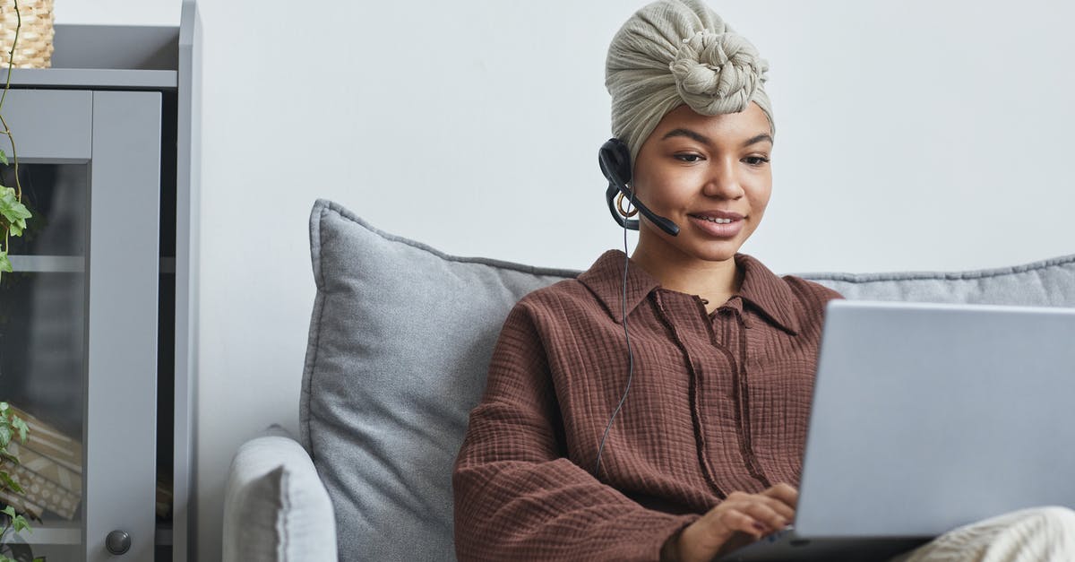 How do you call a local service number, when abroad? - Focused African American female call agent with handsfree headset typing on netbook while sitting on couch near cupboard in light room