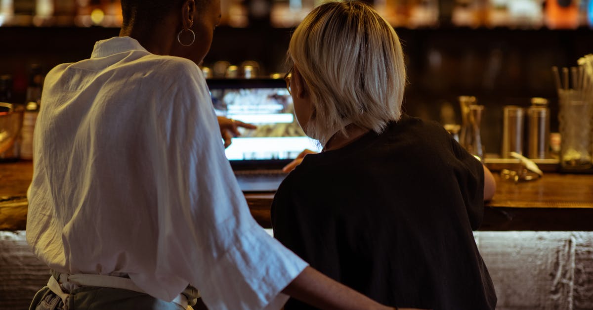 How do you choose a restaurant when travelling? - Back view unrecognizable diverse restaurant workers surfing modern netbook while sitting ar bar counter in cozy restaurant