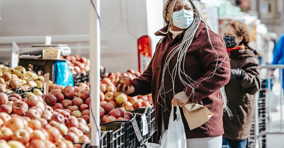 How do you gauge the safety of Indian street food? - Side view of African American lady with braids in warm jacket with bags in hand looking away while choosing fruits near stall on street market