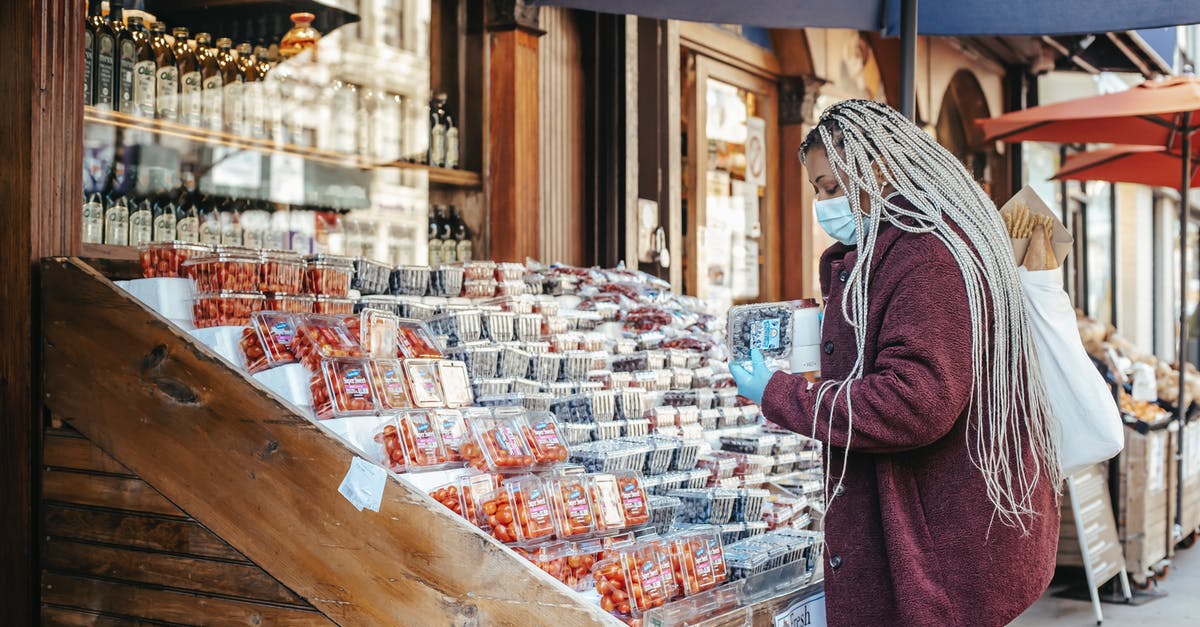 How do you gauge the safety of Indian street food? - Side view of African American female in casual clothes mask and latex gloves standing near street stand with assorted food and choosing blueberries