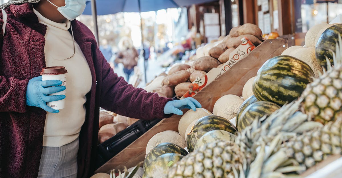 How do you gauge the safety of Indian street food? - Side view of African American female in casual clothes medical mask and latex gloves buying melon in food shop on street