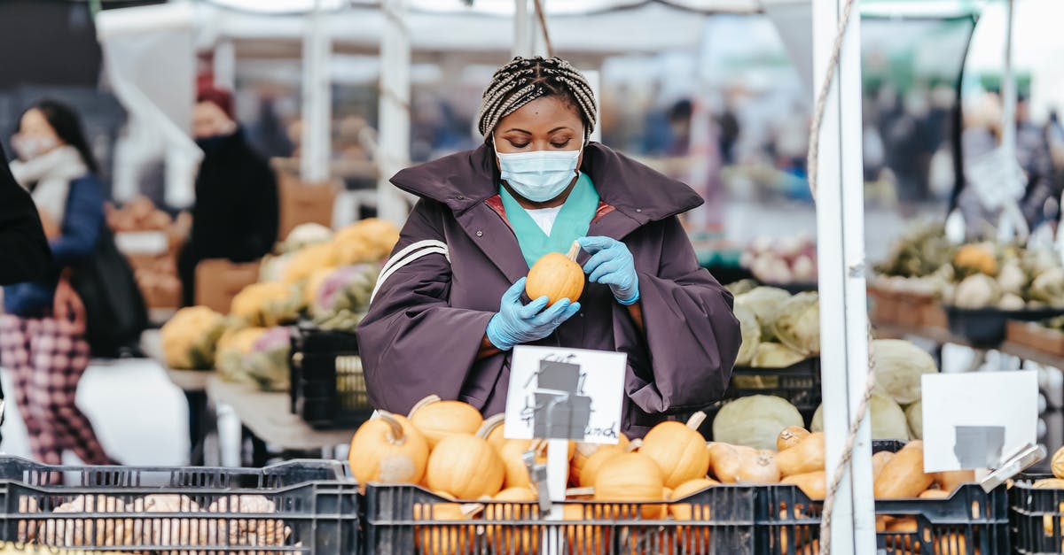 How do you gauge the safety of Indian street food? - Adult African American female nurse in medical uniform and gloves with mask choosing pumpkin from box while standing in daylight in street market