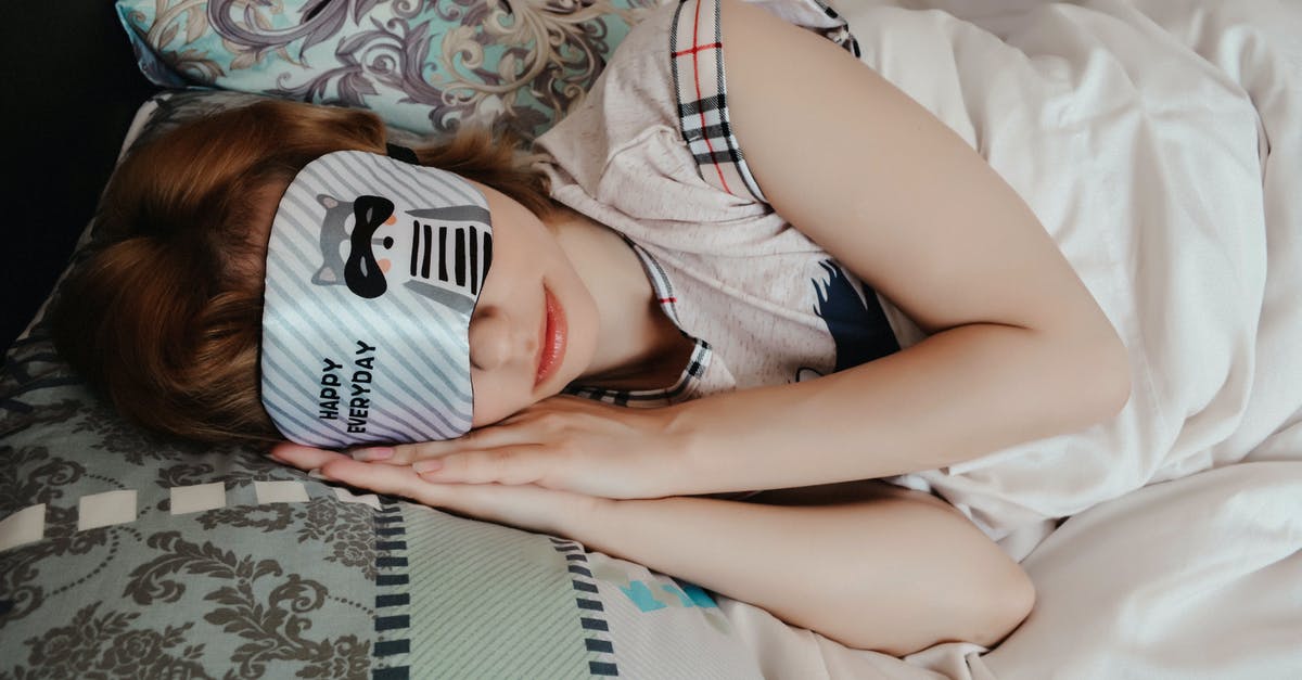 How do you keep a sleep mask on while asleep? - Anonymous female covering eyes with sleep mask taking nap while lying on bed under blanket in cozy bedroom at home