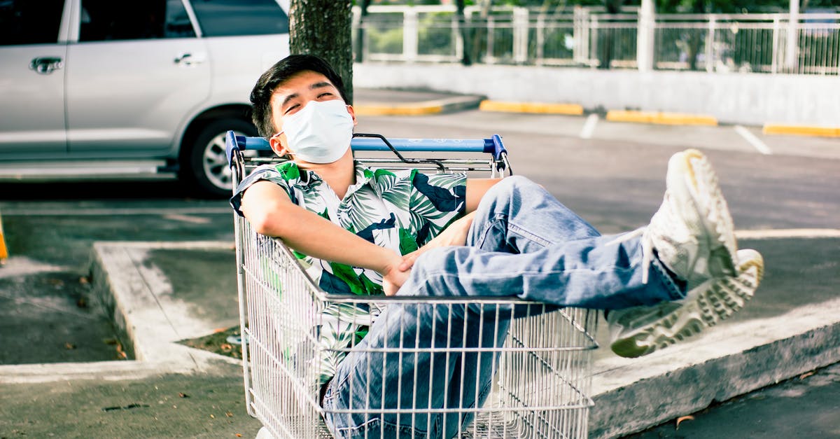 How do you keep a sleep mask on while asleep? - Young Asian man lying in shopping trolley on parking