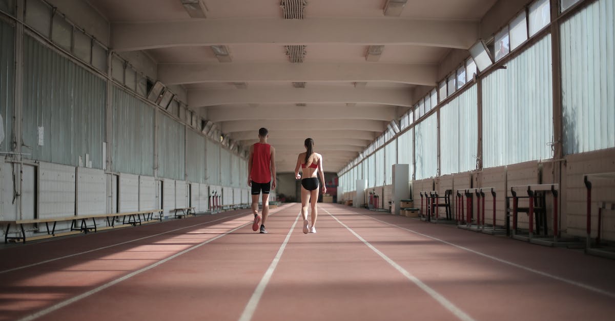 How do you prepare for long haul flights? - Back view of sportsman and sportswoman in activewear walking along running track in athletics arena during warming up before training