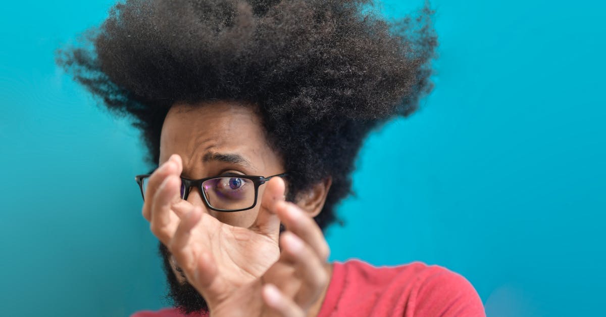 How does airport security search through one's luggage? - Scared young ethnic man looking through hands on blue background in studio