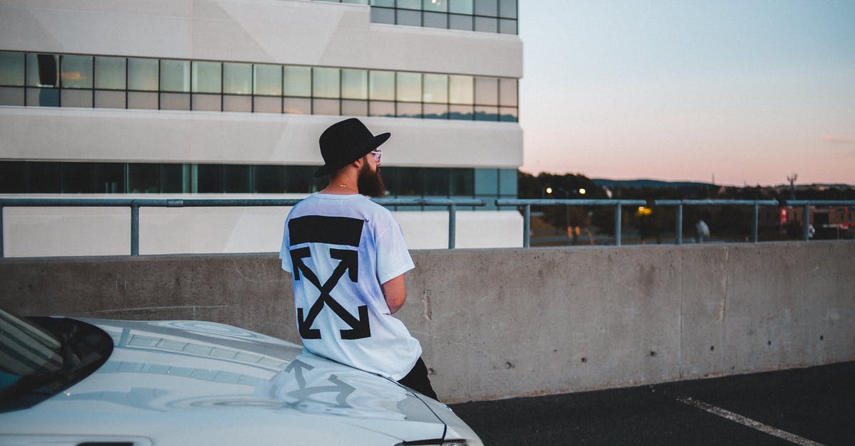 How does the new London T-Charge apply to foreign vehicles? - Back view of trendy anonymous male in stylish T shirt and hat wearing glasses near modern expensive automobile near contemporary building