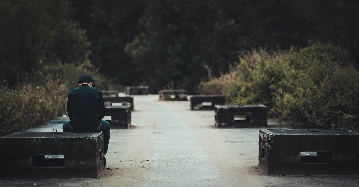 How does the weather compare between Bali and Vietnam in April? - Man in Black Dress Shirt With Blue Denim Shirt Sitting on Black Concrete Bench Near Green Plants