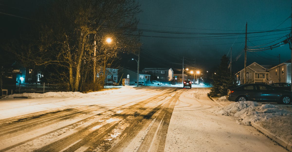 How hard Is it to drive in winter at night in Iceland? - Car driving on roadway with snow and traces against residential houses illuminated by streetlights in night city How hard Is it to drive in winter at night in Iceland? - Car driving on roadway with snow and traces against residential houses illuminated by streetlights in night city