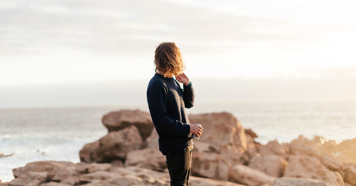 How I can find out about rock concerts in Tallinn? - Side view of anonymous male traveler with can of beverage admiring ocean from rough rocks under shiny sky in evening